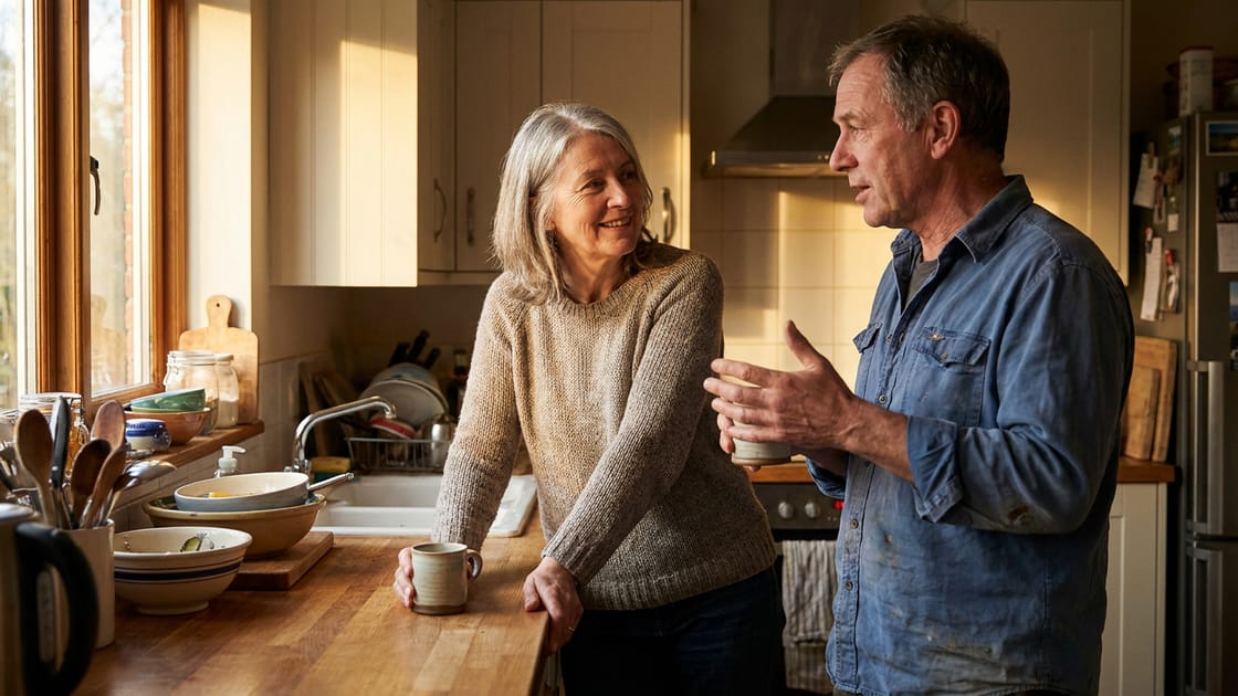 Two people in their sixties talking over coffee at a kitchen counter.